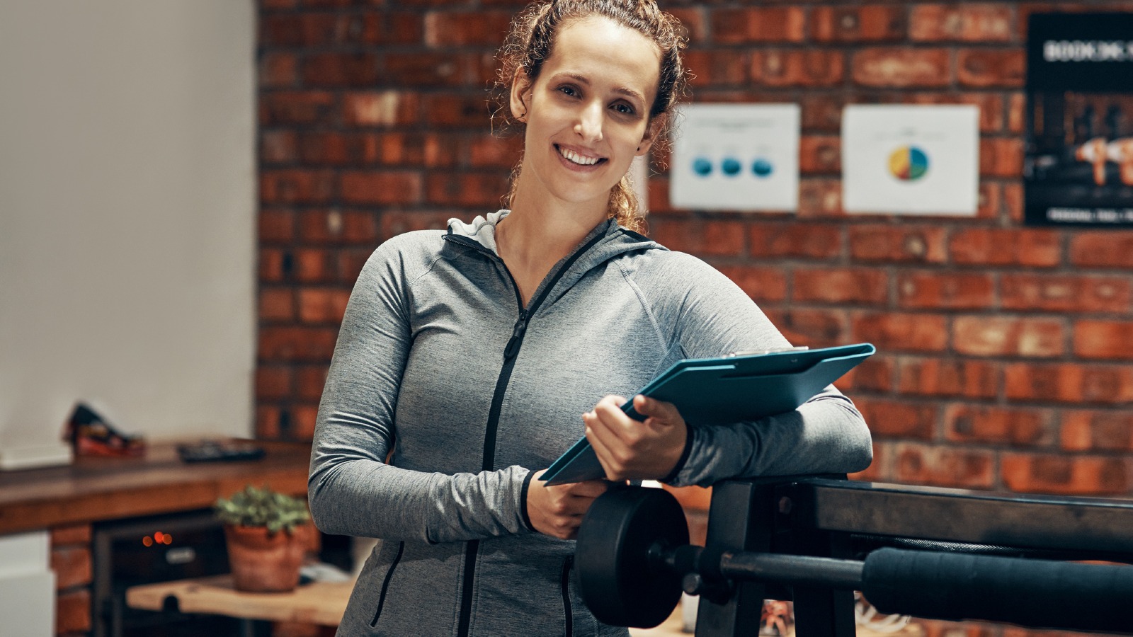 Woman in casual attire standing in a gym or health club holding a clipboard